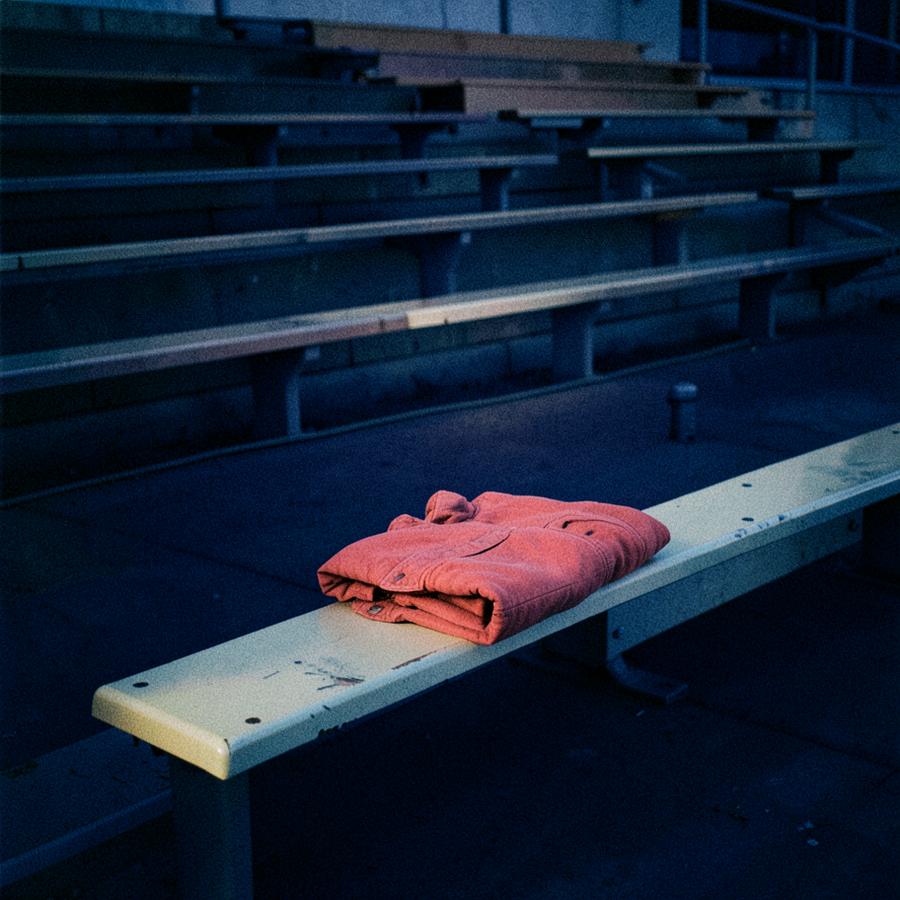 Empty bleachers at dusk with a folded coral jacket left on a bench
