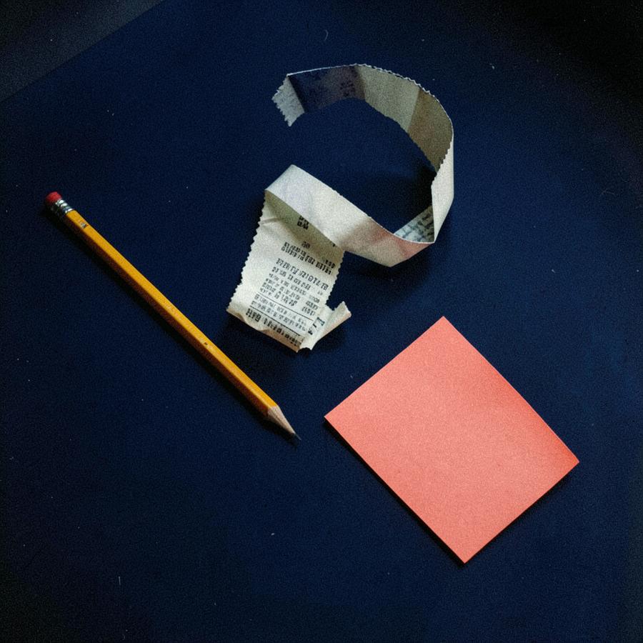 A curled receipt, a pencil and a coral note on a dark navy table